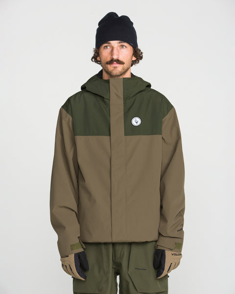 A person wearing the Volcom Men’s Buckthreeeighty Jacket in an olive green and brown baggy fit—crafted with V-Science 2-Layer fabric and PFAS-free DWR—paired with olive pants, a black beanie, and gloves, stands against a plain white background.