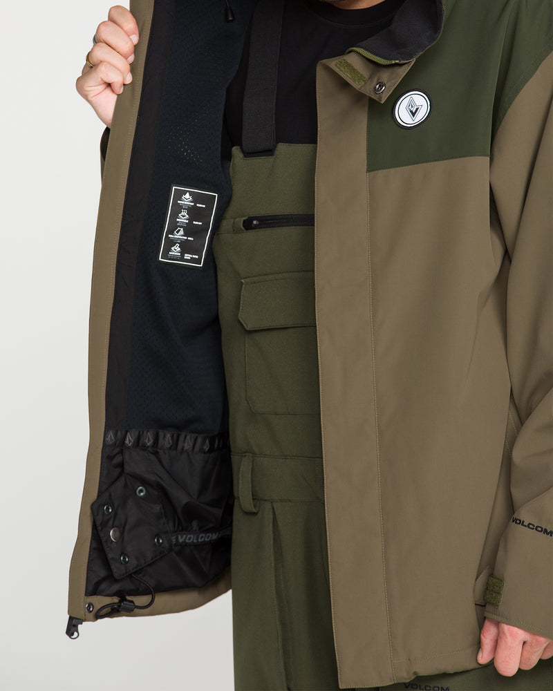 A person wearing the Volcom Men’s Buckthreeeighty Jacket in two-tone green holds it open to display the interior label and pocket details. This baggy fit jacket features a chest patch, Volcom branding on the sleeve, and is crafted with durable V-Science 2-Layer construction for reliable performance.