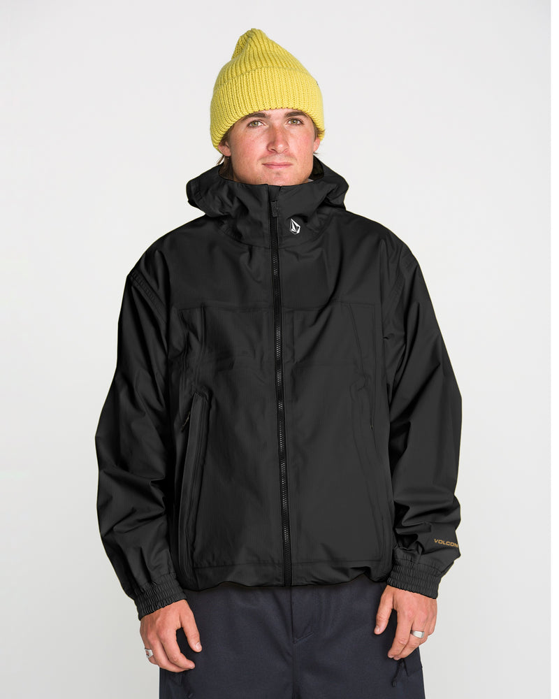 A person wearing a yellow knit beanie and the Volcom Men’s Arthur 3L 20K Jacket stands facing forward against a plain white background.