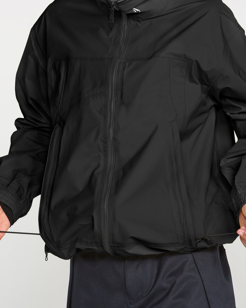 A person wearing the Volcom Men’s Arthur 3L 20K Jacket adjusts the elastic drawstring at the hem. Only the torso and portions of the arms and pants are visible, emphasizing storm-level protection and advanced V-Science 3-Layer technology.