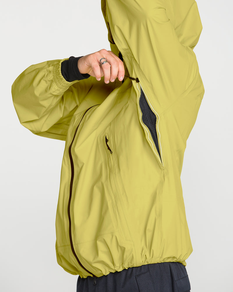 A person wearing a Volcom Men’s Arthur 3L 20K Jacket in light green unzips a side ventilation opening under the arm. Featuring V-Science 3-Layer construction, this jacket includes a front zipper and elastic cuffs for storm-grade protection. Only the torso and arm are visible.