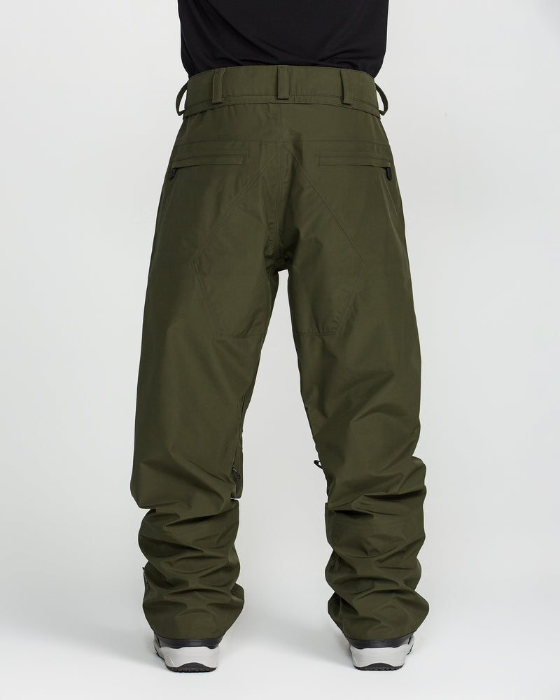 A person is photographed from the back against a plain white background wearing Volcom’s Unisex Tester 3L Gore-Tex Pants in olive green, inspired by waterproof ski pants and featuring belt loops and multiple pockets. They are paired with gray sneakers.