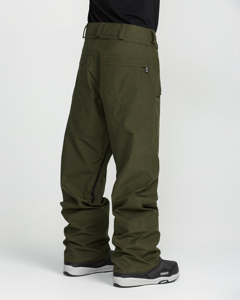 A person is shown from the back against a plain white background, wearing Volcom Unisex Tester 3L Gore-Tex Pants in olive green. The loose-fitting, waterproof ski pants feature back pockets, a side zipper, and are paired with black boots.