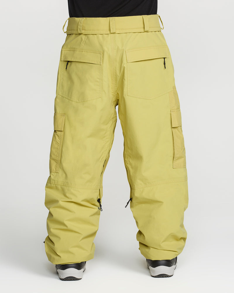 A person is wearing Volcom Men’s Longo Gore-Tex Pants—loose-fitting yellow snowboard pants inspired by Arthur Longo, featuring multiple pockets and black zipper details—paired with black shoes. The plain white background highlights the GORE-TEX design and fit of these Volcom pants.