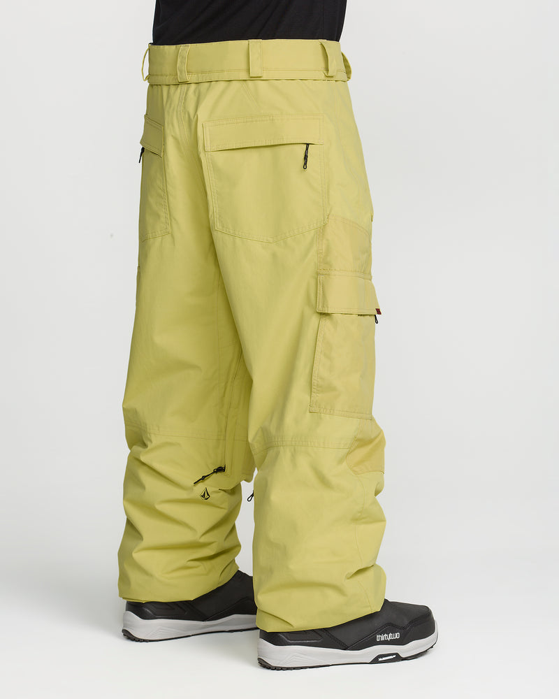 Wearing Volcom’s Men’s Longo Gore-Tex Pants in a relaxed, light yellow cut with multiple pockets and pairing them with black sneakers, this individual stands against a plain white background—channeling Arthur Longo’s signature style.