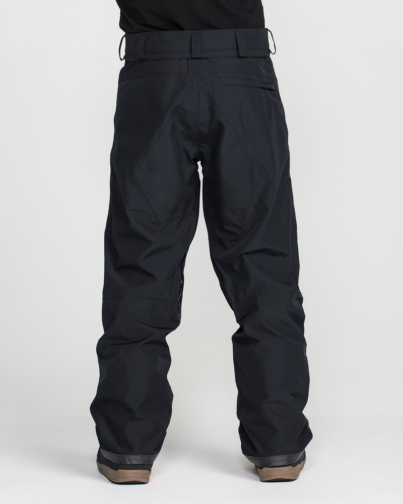 A person is shown from the back against a plain white background, wearing loose-fitting black Volcom Men’s Dua Gore-Tex Pants and brown boots. These waterproof pants feature belt loops, reinforced stitching on the back, and a breathable lining for added comfort.