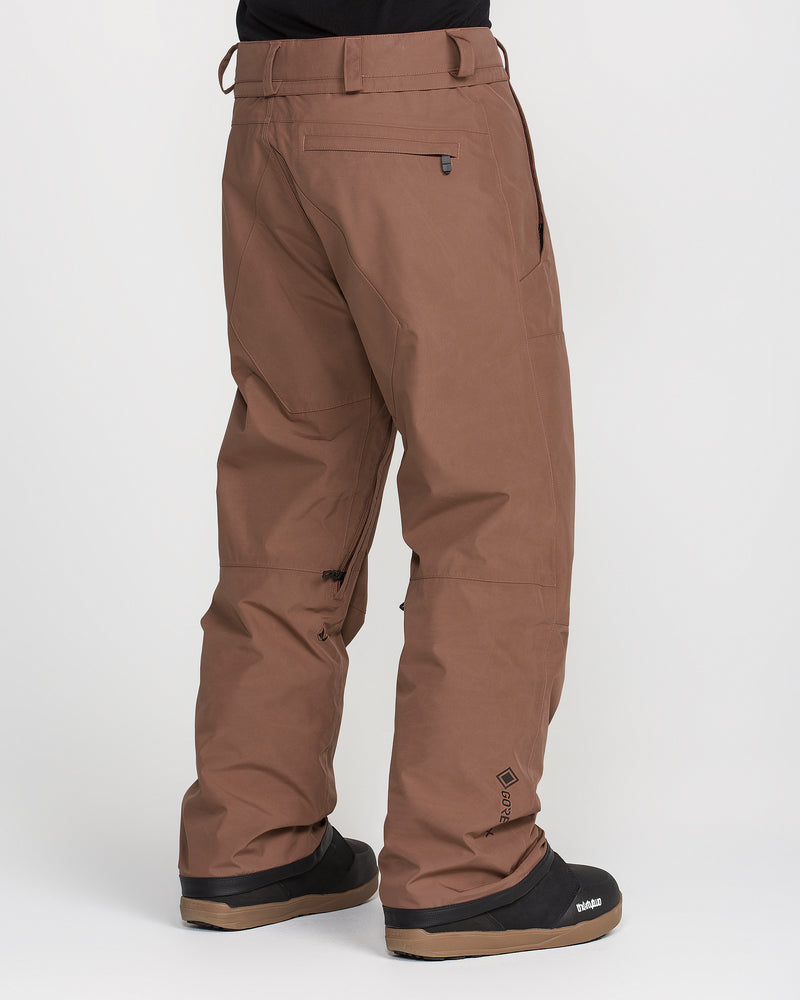 A person is photographed from the back against a plain white background wearing Volcom Men’s Dua Gore-Tex Pants—loose-fitting, waterproof snow pants with a breathable lining—paired with black snow boots.