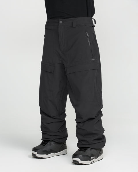 A person is shown from the waist down wearing Volcom Men’s Rnge Stretch 30K Pants in black, paired with black sneakers, standing against a white background.