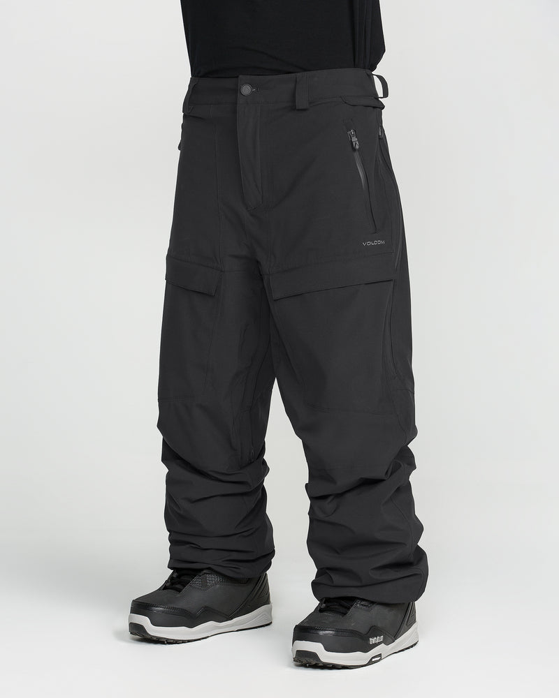 A person is shown from the waist down wearing Volcom Men’s Rnge Stretch 30K Pants in black, paired with black sneakers, standing against a white background.