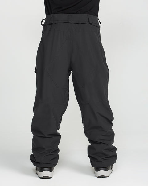 A person wears the Volcom Men’s Rnge Stretch 30K Pants in black, paired with silver sneakers and stands with legs slightly apart against a plain white background; only the lower half of the body is visible.