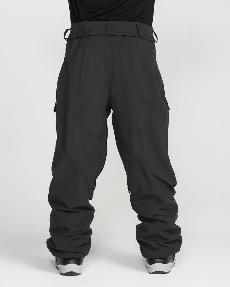 A person wears the Volcom Men’s Rnge Stretch 30K Pants in black, paired with silver sneakers and stands with legs slightly apart against a plain white background; only the lower half of the body is visible.