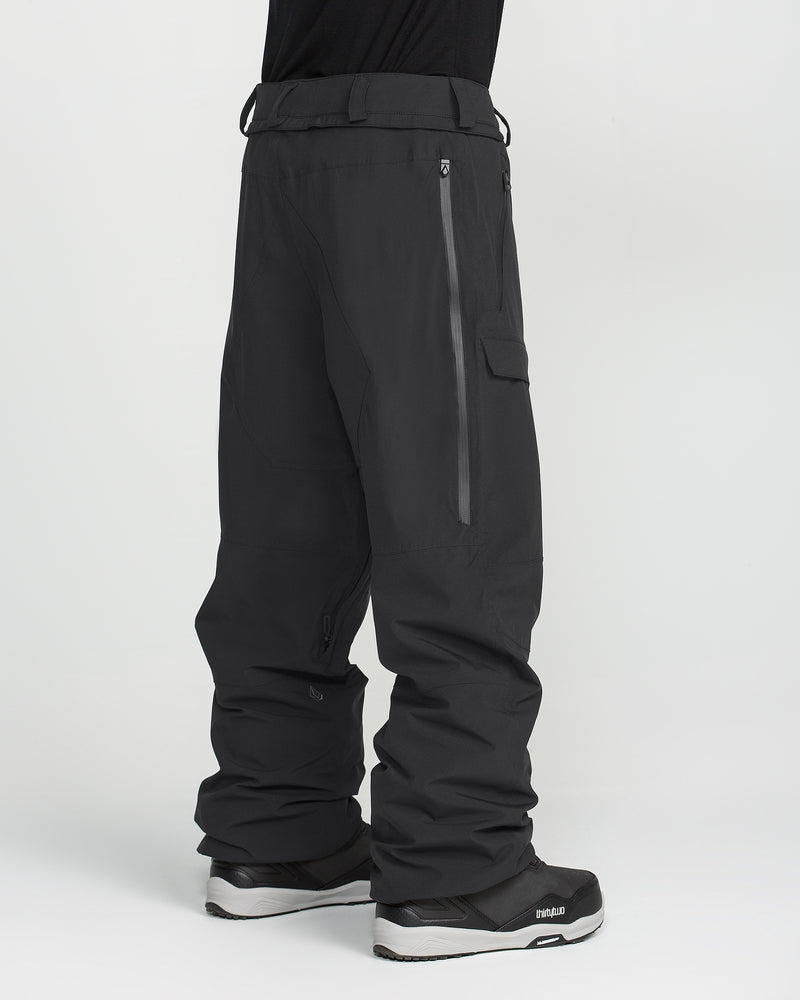 A person is shown from the waist down wearing Volcom Men’s Rnge Stretch 30K Pants in black, featuring zippered pockets, paired with black boots. The background is plain white.