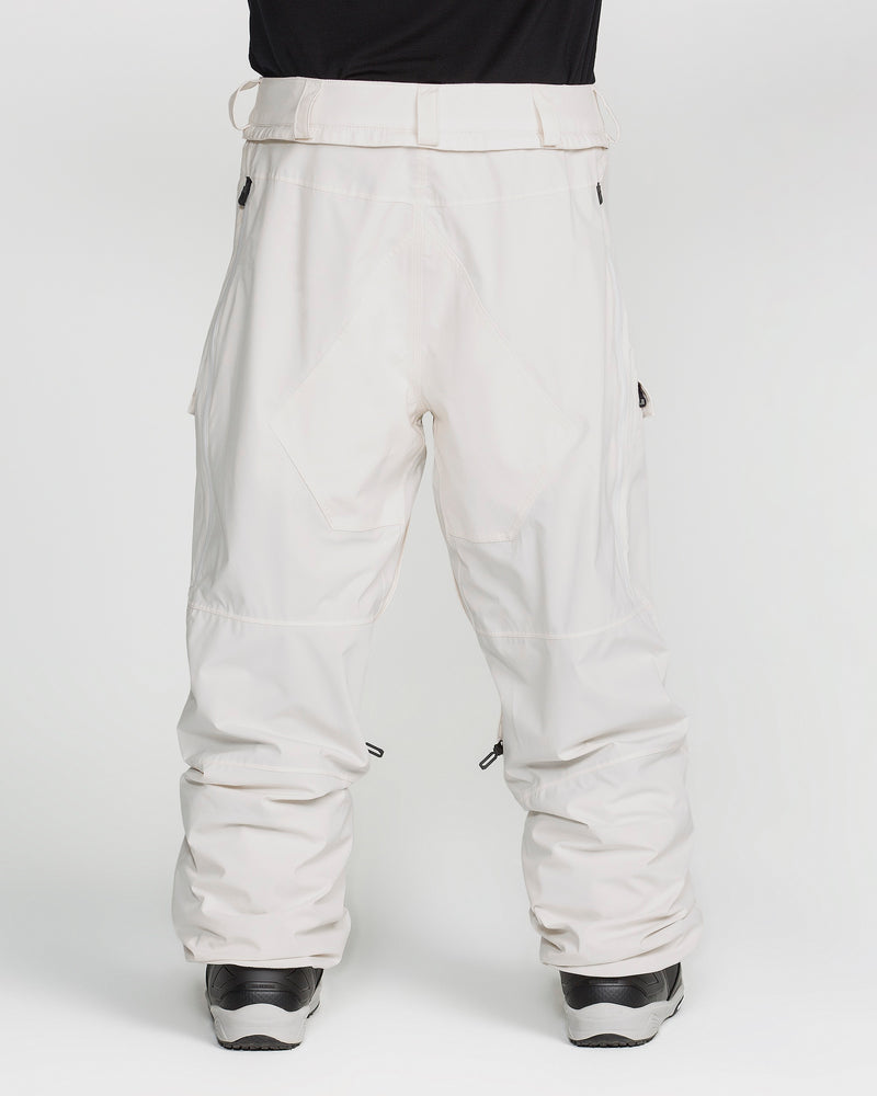 A person is wearing the Volcom Men’s Rnge Stretch 30K Pants in a loose, baggy fit white design, paired with black boots and standing against a plain white background. These pants feature side pockets, a high waist, and provide comfortable 4-way stretch for easy movement.