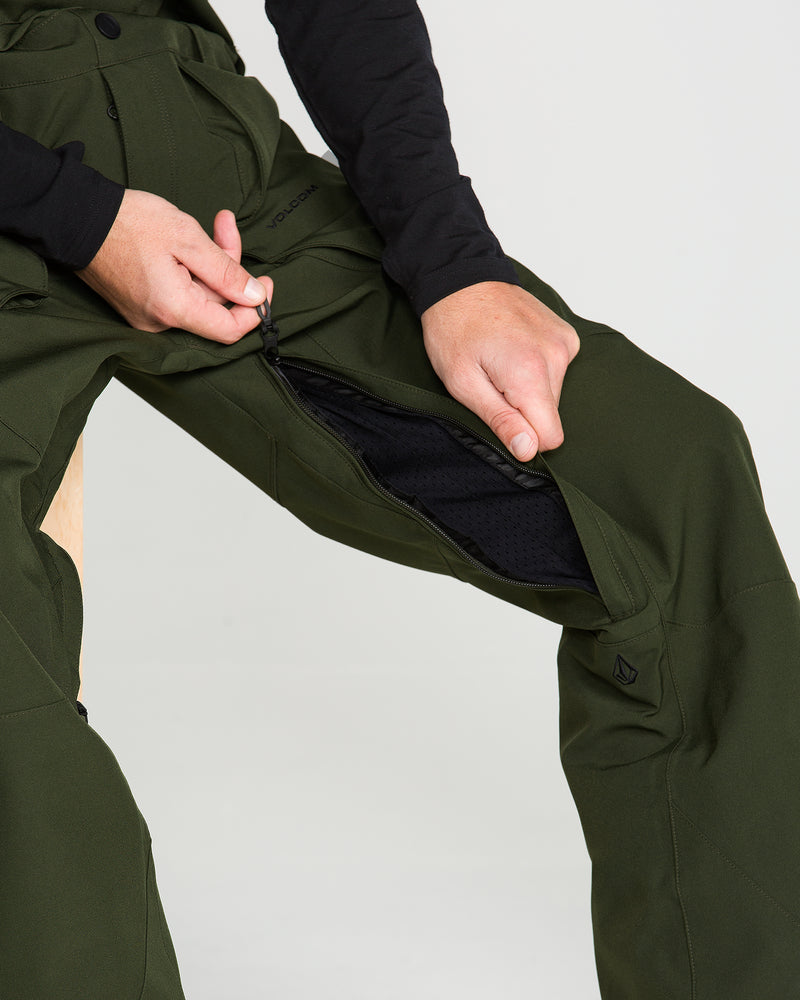 A person unzips a thigh vent on green Volcom Men’s Roan Bib pants while seated, exposing a black mesh lining that highlights the premium recycled stretch Oxford fabric and 15K protection of this outdoor bib.