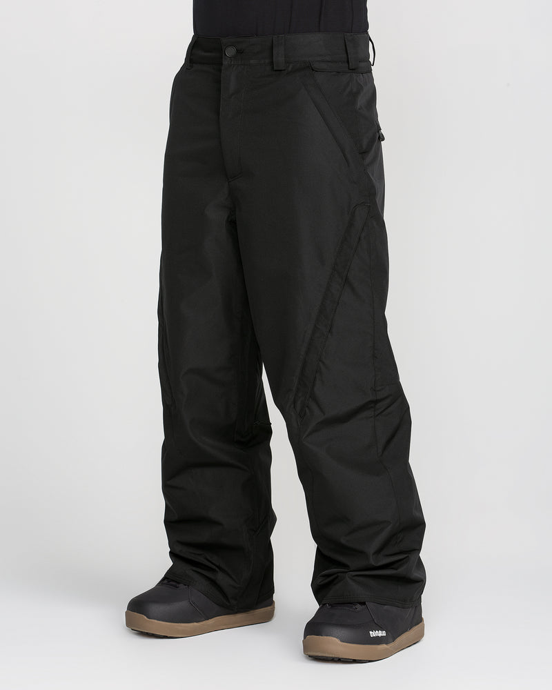 A person is wearing baggy black Volcom Men’s Kleveland Pants and black snow boots with brown soles, standing against a plain light background. Only the lower half of the body is visible in the image.