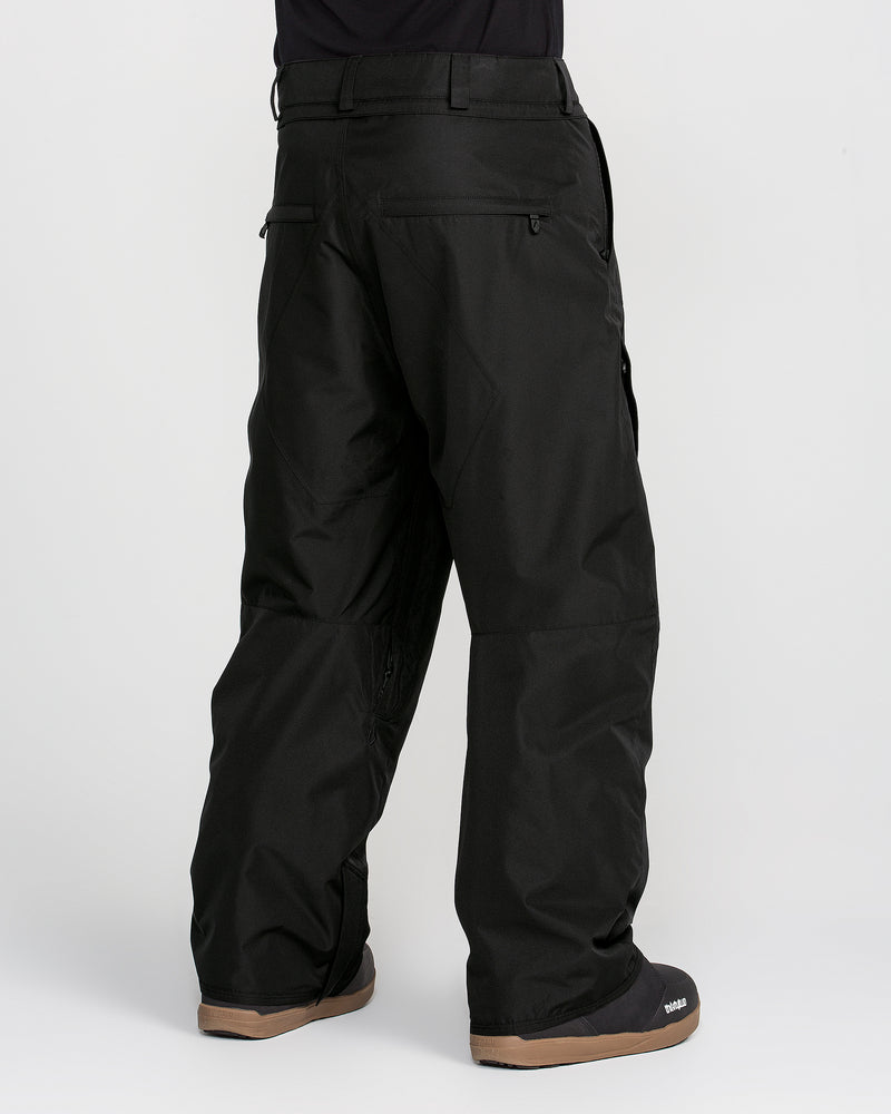 A person is shown from the back against a plain white background, wearing Volcom Men’s Kleveland Pants—loose-fitting black pants reminiscent of baggy snow pants—and black boots with tan soles.