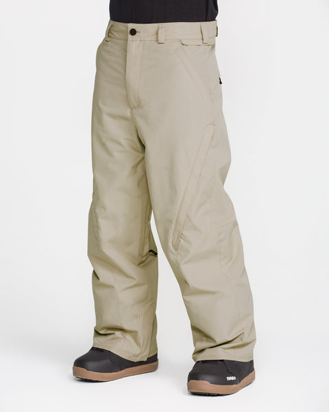 A person is wearing the Volcom Men’s Kleveland Pants in a loose, baggy beige fit, paired with black winter boots, standing against a plain white background.