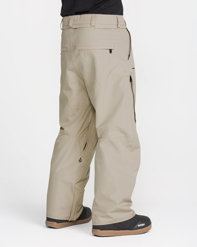 A person wearing Volcom Men’s Kleveland Pants in light beige, paired with black boots, is photographed from behind against a white background.