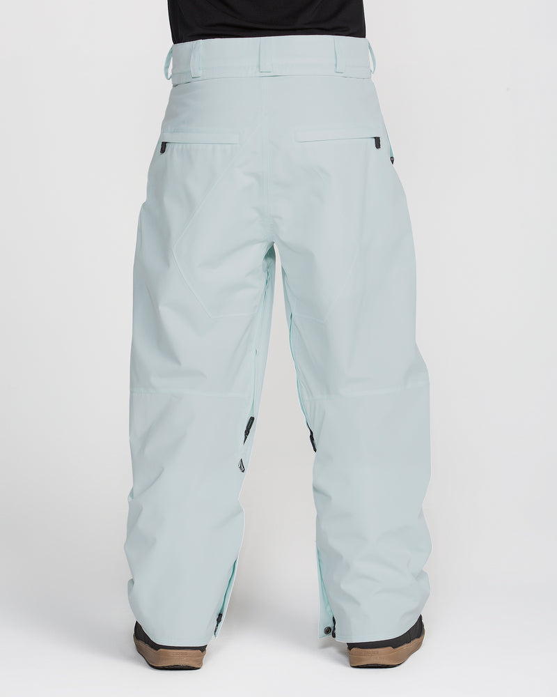 A back view of a person wearing Volcom Men’s Kleveland Pants in light blue with brown boots, standing against a plain white background.