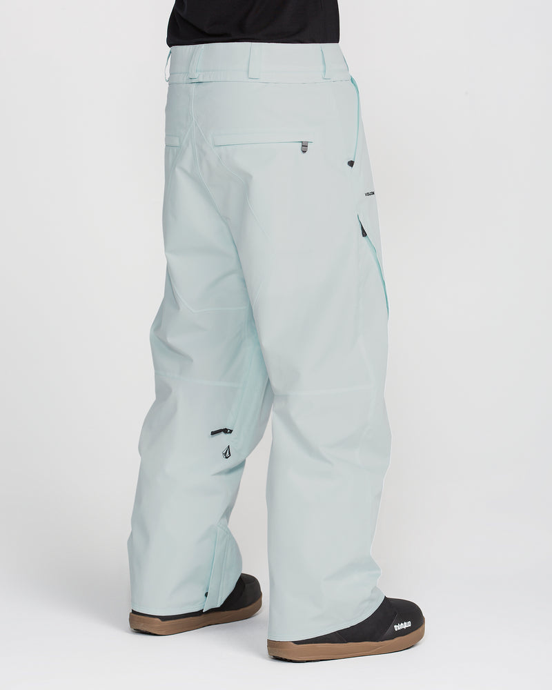 A person wearing Volcom Men’s Kleveland Pants in light blue, featuring a baggy fit, multiple zippered pockets, and distinctive seams reminiscent of Marcus Kleveland’s style, paired with black boots. The photo is taken from the back on a white background, showing only the lower body.