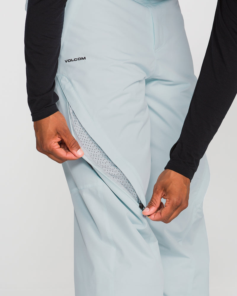 A person wearing Volcom Men’s Kleveland Pants in light blue unzips a ventilated side pocket, revealing mesh lining. Only the lower torso and hands are visible.