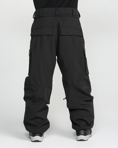 A man is seen from the back, standing against a plain white background, wearing Volcom Men’s Nwrk 20K Baggy Pants—loose-fitting black cargo pants made from recycled shell fabric, featuring multiple pockets and a baggy silhouette.