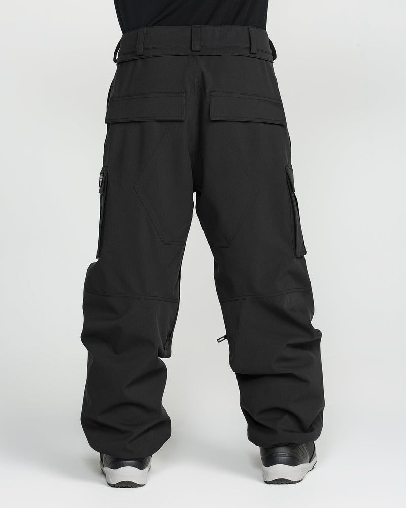 A man is seen from the back, standing against a plain white background, wearing Volcom Men’s Nwrk 20K Baggy Pants—loose-fitting black cargo pants made from recycled shell fabric, featuring multiple pockets and a baggy silhouette.