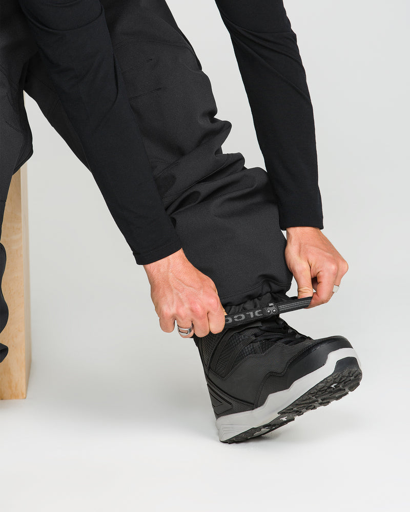 Seated on a wooden bench, a person in Volcom’s Men’s Nwrk 20K Baggy Pants and boots tightens a strap around their ankle—the pants’ recycled shell balancing sustainability with style.
