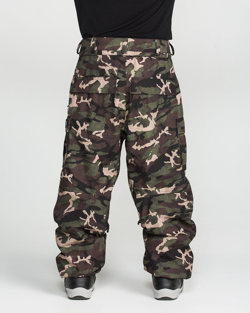 A person wearing Volcom Men’s Nwrk 20K Baggy Pants and black sneakers stands against a plain white background, with only the lower half of their body visible.