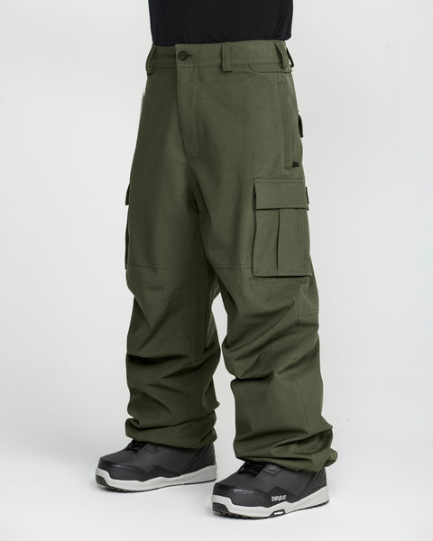 A person stands against a plain white background wearing the Volcom Men’s Nwrk 20K Baggy Pants in olive green and black snow boots; these men’s snow pants feature a 20K waterproof finish.