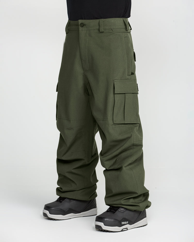 A person stands against a plain white background wearing the Volcom Men’s Nwrk 20K Baggy Pants in olive green and black snow boots; these men’s snow pants feature a 20K waterproof finish.