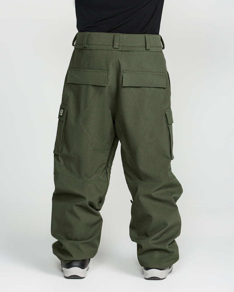 A person is shown from the back against a plain white background wearing Volcom Men’s Nwrk 20K Baggy Pants—loose-fitting olive green cargo pants with multiple pockets, reminiscent of snow pants—paired with sneakers and a partially visible black top.