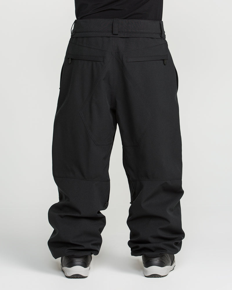 A person is shown from the back against a plain white background, wearing Volcom Men’s Snow Billow Pants in black featuring V-Science 2-Layer construction and 10K waterproof protection, paired with gray sneakers.