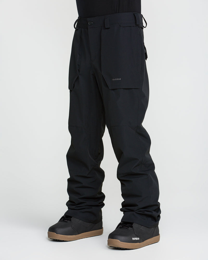 A person is wearing black Volcom Men’s Roan 20K Pants and black winter boots, standing against a plain white background. Only the lower half of the body is visible.
