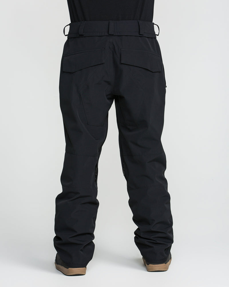 A person shown from the back against a plain white background is wearing Volcom Men’s Roan 20K Pants in black and brown shoes.