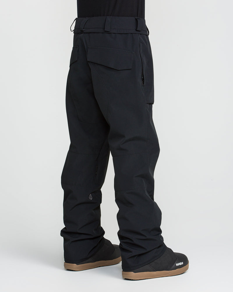 A person wearing loose-fitting black Volcom Men’s Roan 20K Pants made from recycled fabric, featuring flap pockets, is shown standing sideways against a plain white background. The 20K waterproof pants look insulated, breathable, and ideal for winter or outdoor activities. Black snow boots complete the outfit.