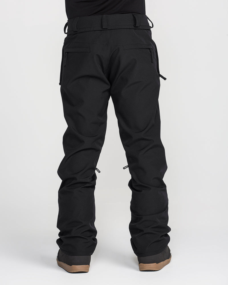 A person stands facing away, showcasing the Volcom Men’s Freakin Snow Chino Pants in black with brown boots against a plain white background. Only the lower body is visible, emphasizing the waterproof and breathable fabric of these men’s ski pants.