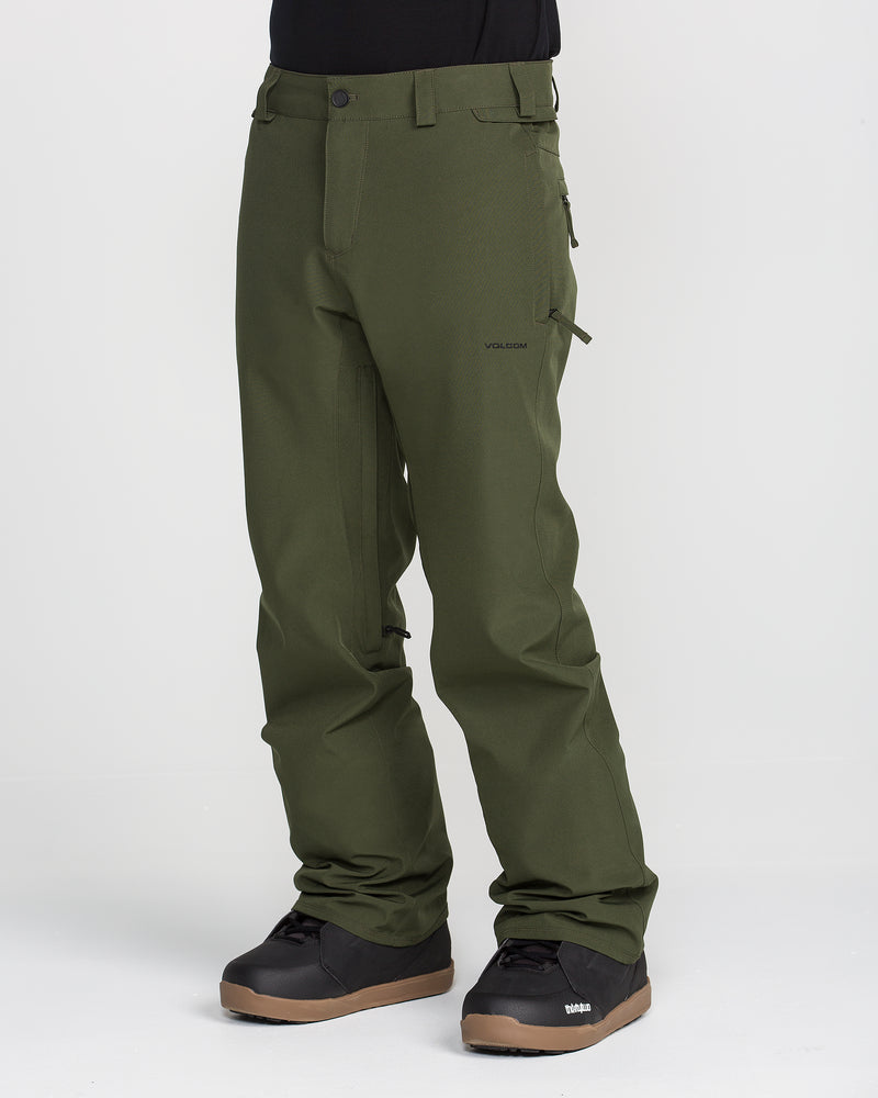 A person wearing olive green Volcom Men’s Freakin Snow Chino Pants and black boots stands against a plain white background. The men’s snow pants feature a side pocket and are constructed from a durable, waterproof, and breathable material.