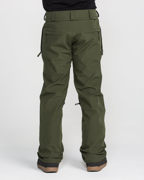 A person wearing olive green Volcom Men’s Freakin Snow Chino Pants, renowned for their waterproof breathable fabric, and brown-soled shoes stands facing away to showcase the back view of these men’s snow pants against a plain white background.