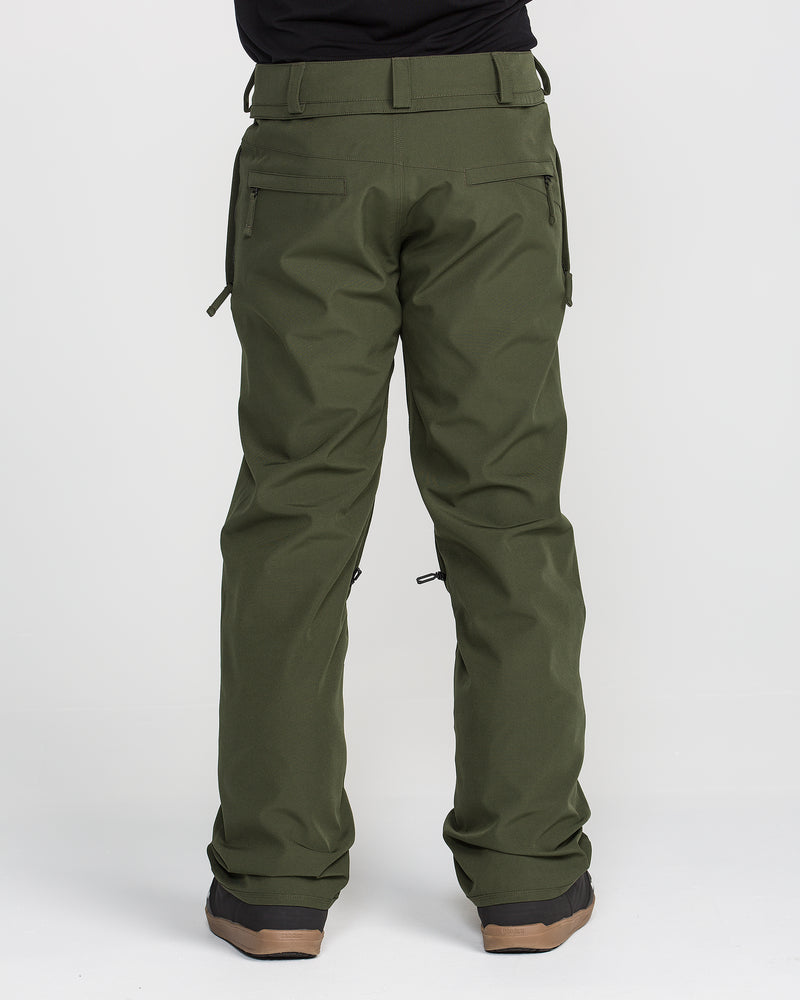 A person wearing olive green Volcom Men’s Freakin Snow Chino Pants, renowned for their waterproof breathable fabric, and brown-soled shoes stands facing away to showcase the back view of these men’s snow pants against a plain white background.