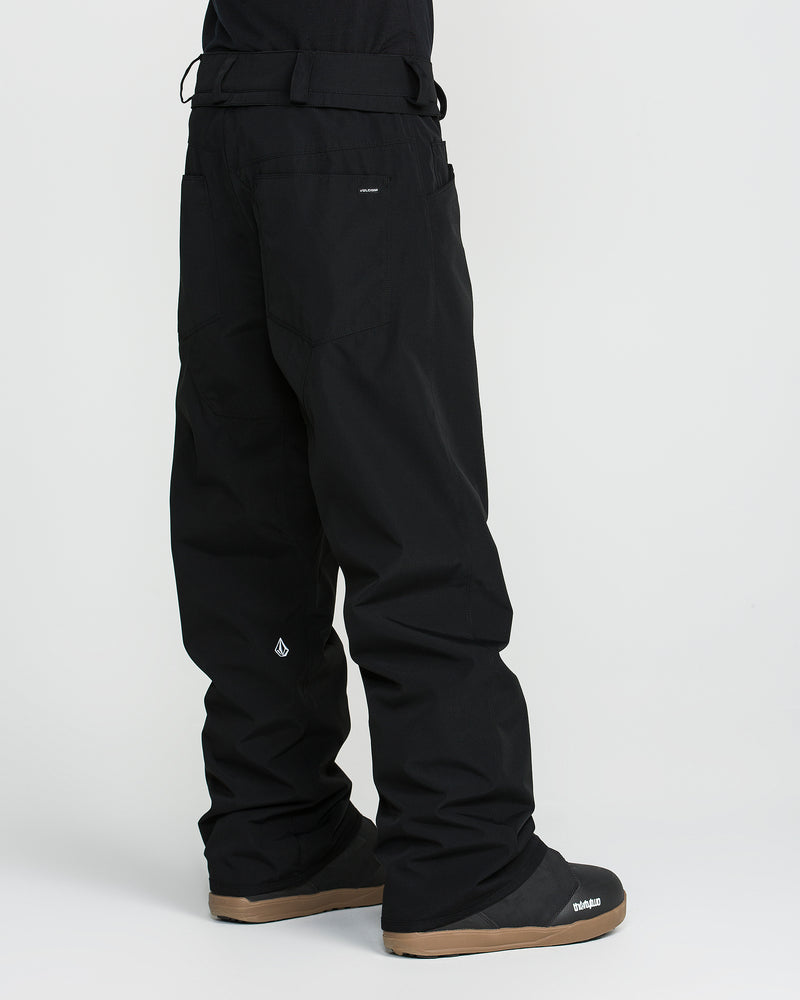 A person is shown wearing loose black Volcom Men’s Nailer Pants and black boots with tan soles, standing against a plain white background. Only the lower half of their body is visible. These waterproof pants from Volcom are crafted from recycled materials, combining style with sustainability.
