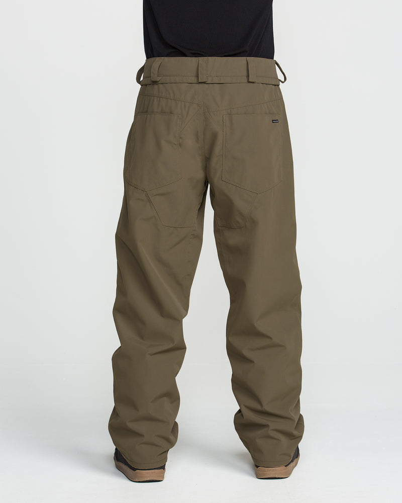 A person is seen from the back wearing Volcom Men’s Nailer Pants in olive green, featuring a loose fit with two rear pockets and belt loops. The pants are paired with a black shirt and black shoes.