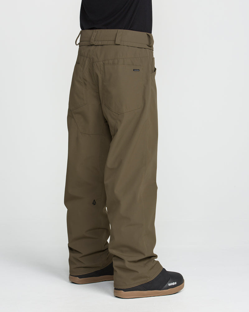 A person wearing loose-fitting olive green Volcom Men’s Nailer Pants, which feature belt loops and back pockets, and black snow boots, shown from the side and back against a plain white background.