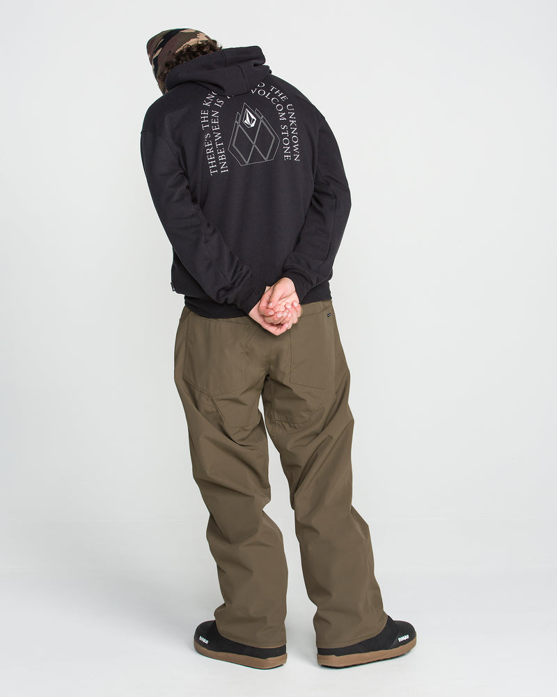 A person in a black hoodie with a white graphic and brown pants stands facing away, hands clasped behind their back, wearing a camo beanie and black shoes against a plain white background—the look is completed with Volcom Men’s Nailer Pants, designed for urban style and mountain-ready comfort.