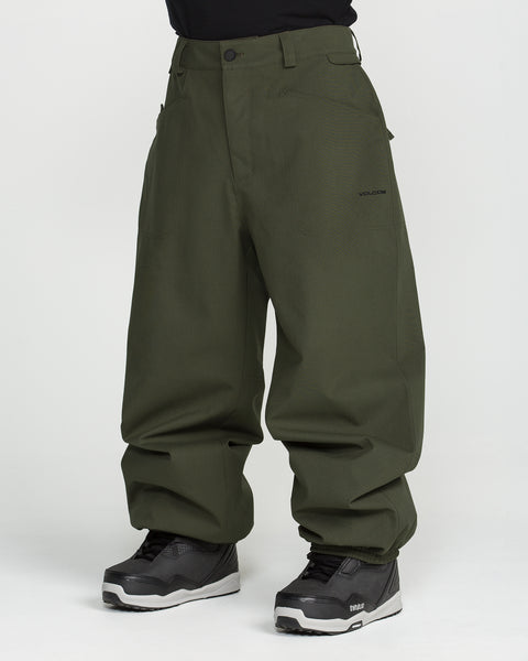 A person wearing Volcom Men’s Lapper Pants in a loose-fitting, dark green style paired with black sneakers, standing against a plain white background. Only the lower half of the body is visible.