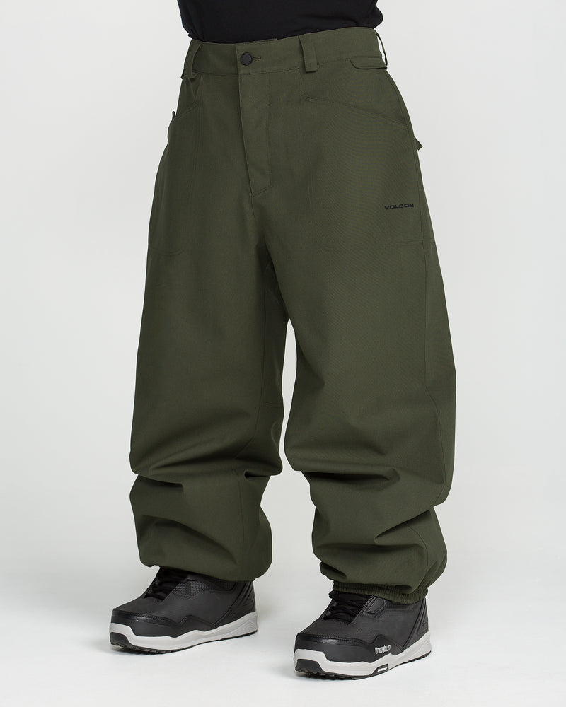 A person wearing Volcom Men’s Lapper Pants in a loose-fitting, dark green style paired with black sneakers, standing against a plain white background. Only the lower half of the body is visible.