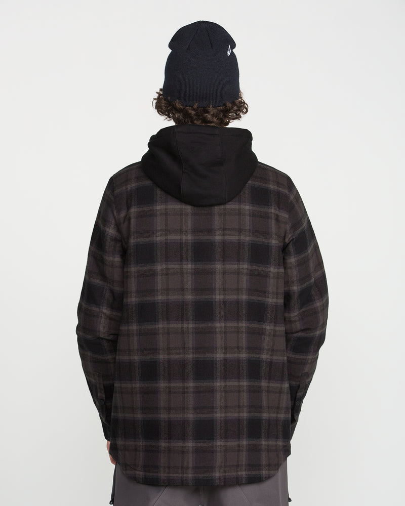A person is standing with their back to the camera against a plain white background, wearing a black beanie, a fleece hood, and the Volcom Men’s Enson Insulated Riding Flannel.