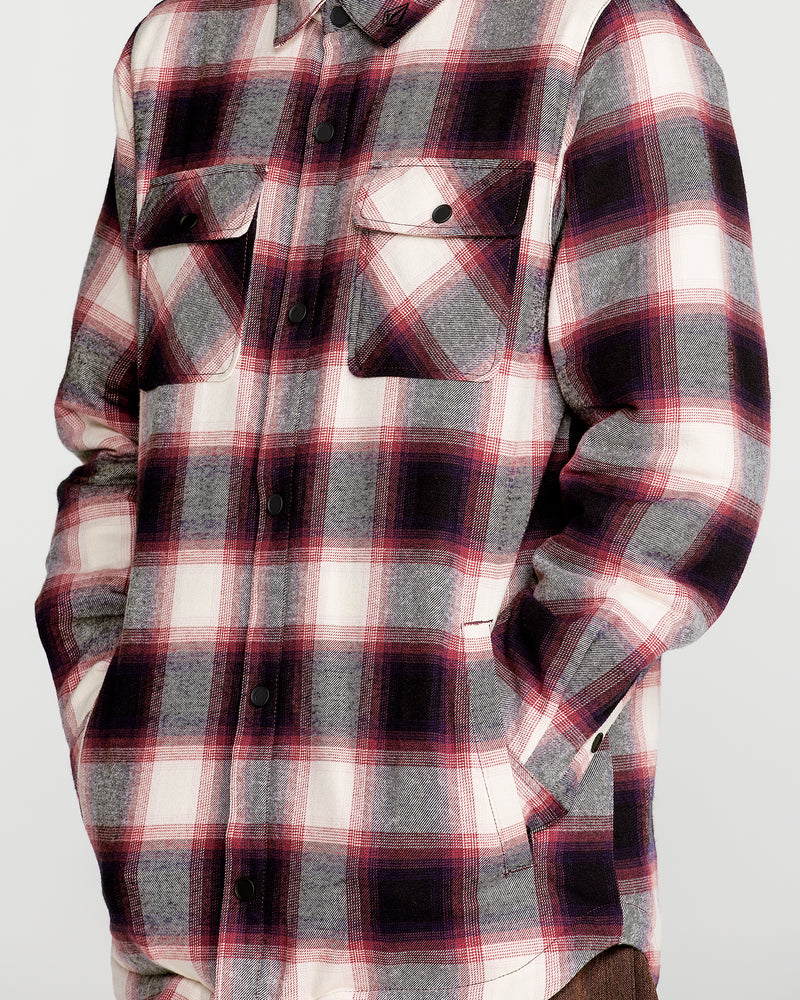 A person is wearing the Volcom Men’s Enson Insulated Riding Flannel, featuring a red, black, and white plaid pattern. This long-sleeve flannel shirt has buttoned front closure and two chest pockets with buttoned flaps. The individual has their hands in their pockets.