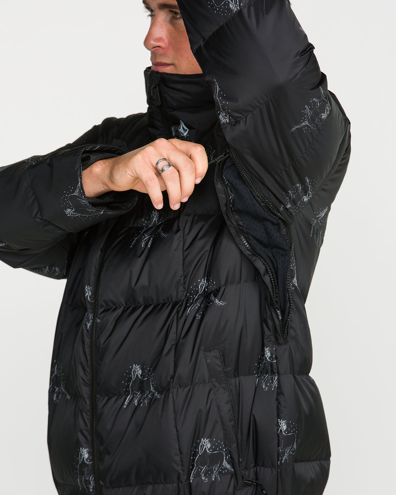 A person wearing the Volcom Men’s Arthur Down Puff Jacket in black, featuring white prints and a baggy fit, unzips an underarm vent to reveal the jacket’s interior lining.