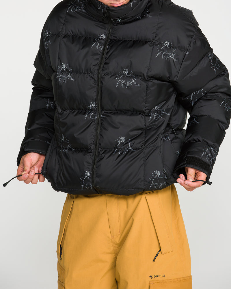 A person wearing the Volcom Men’s Arthur Down Puff Jacket in a baggy fit with subtle prints and black color, paired with tan GORE-TEX pants, is holding the jacket’s drawstrings. The PFAS-free DWR finish offers added protection, while the person’s face is partially out of frame.